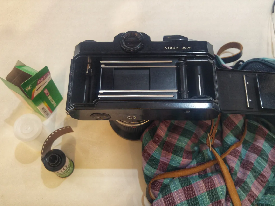 A Nikon film camera and a roll of film laid out on a checked cloth
