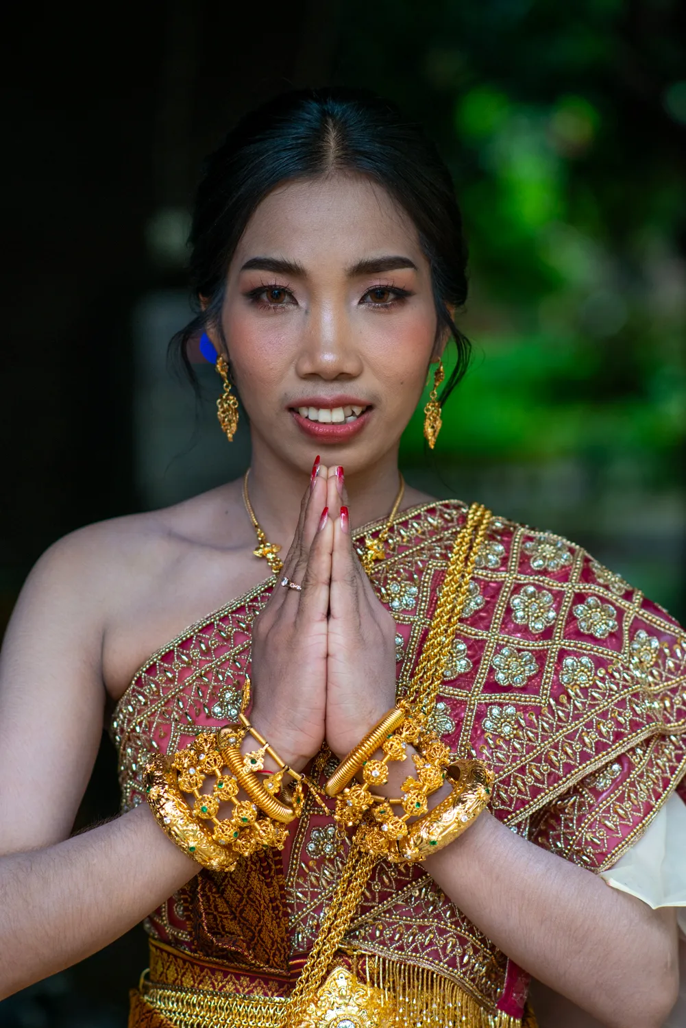 Woman in traditional Khmer dress and gold jewellery, hands together in a sampeah greeting