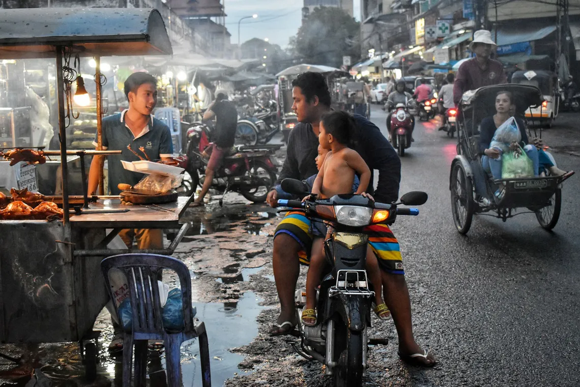Street food stall and motorbikes in a busy Phnom Penh street at dusk